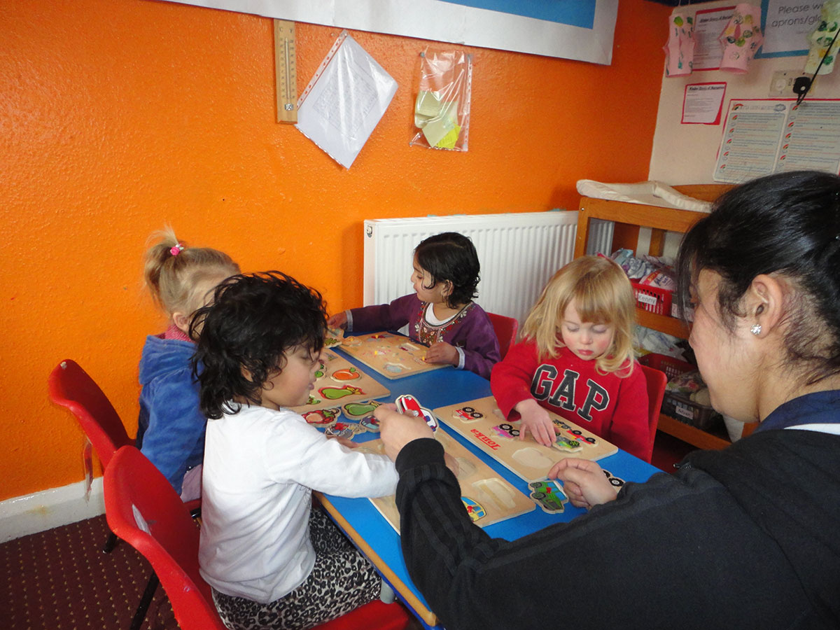 Children playing with jigsaws with a nursery assistant