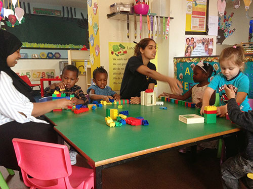 Some children and two nursery assistants playing with bricks at a table