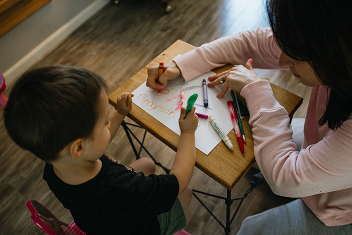 Young boy sitting at table crayoning with an adult woman